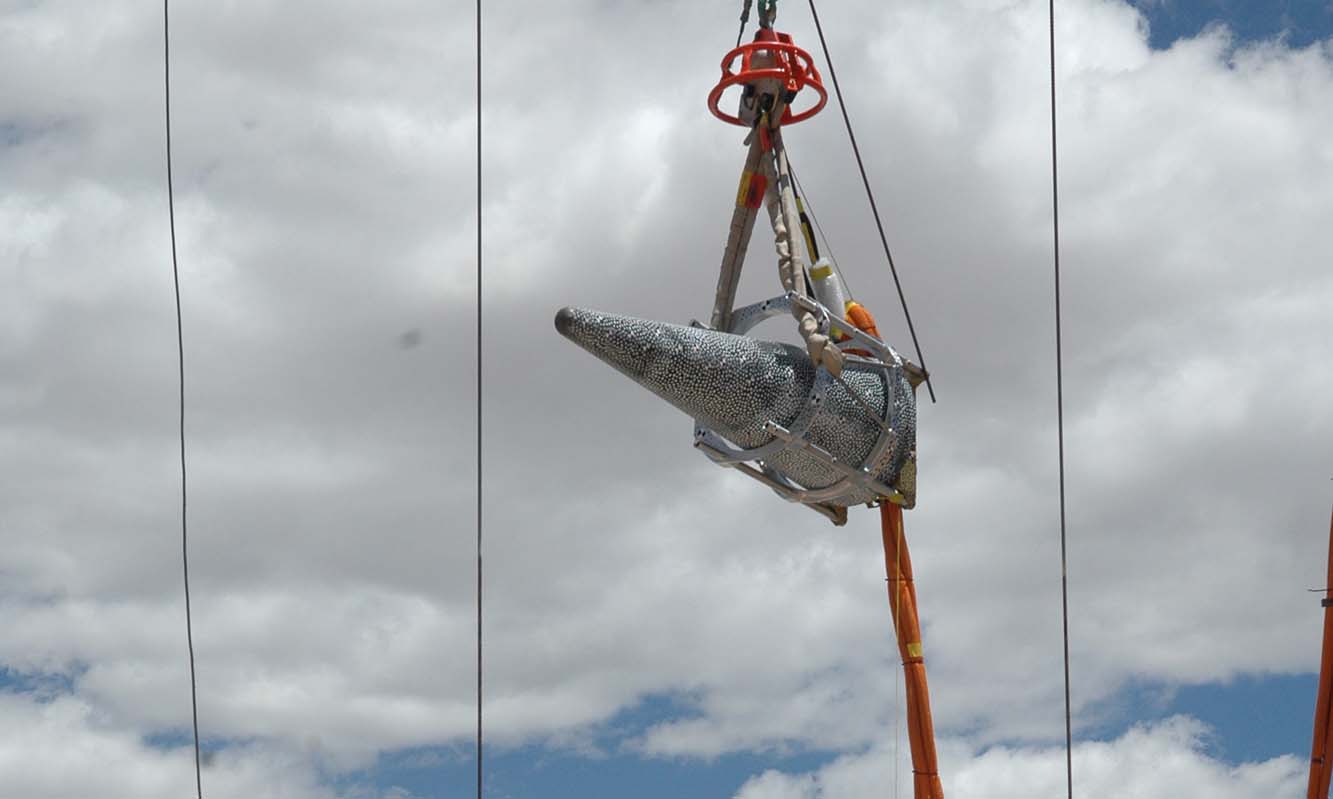 A nose cone is lifted into the air by a crane for a drop test.