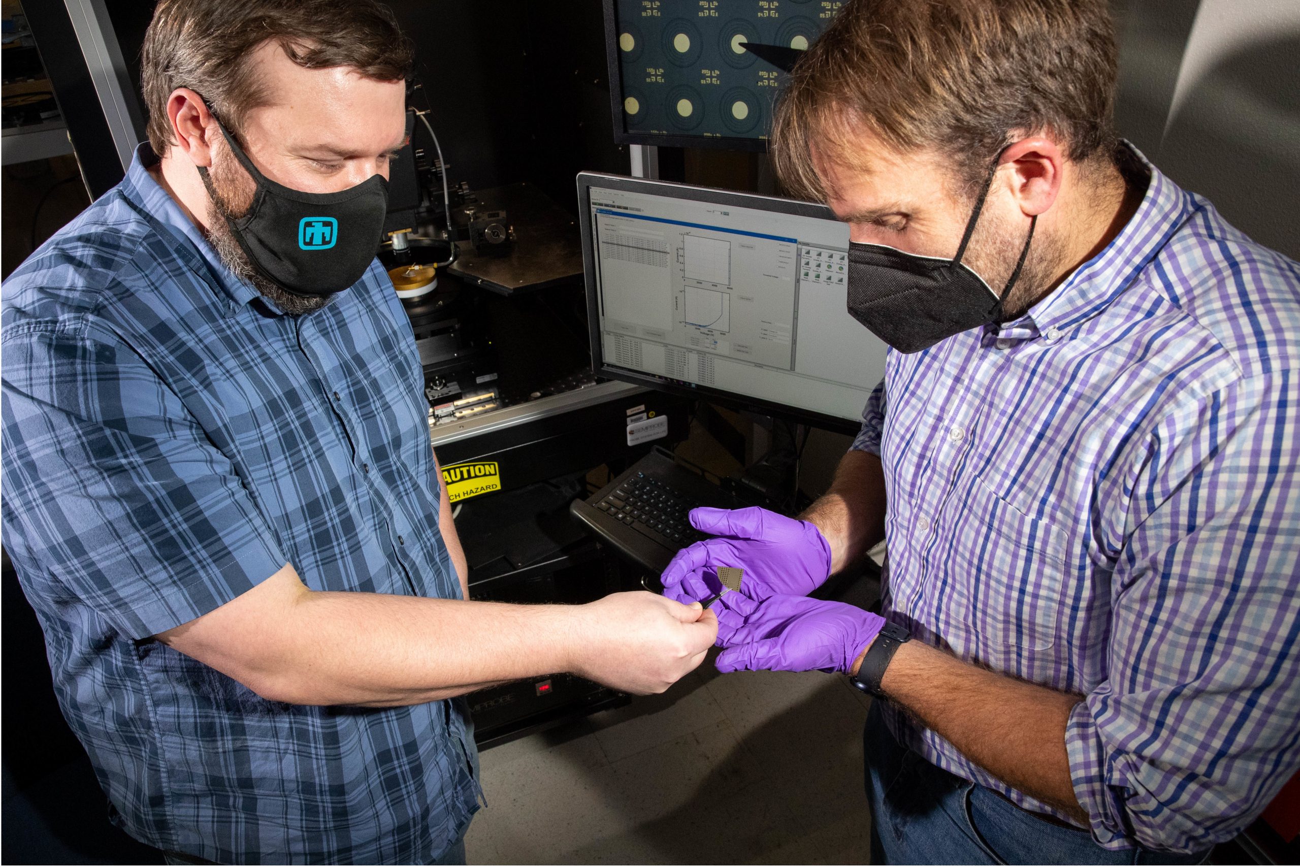Luke Yates and Jack Flicker look at a tiny gallium nitride wafter