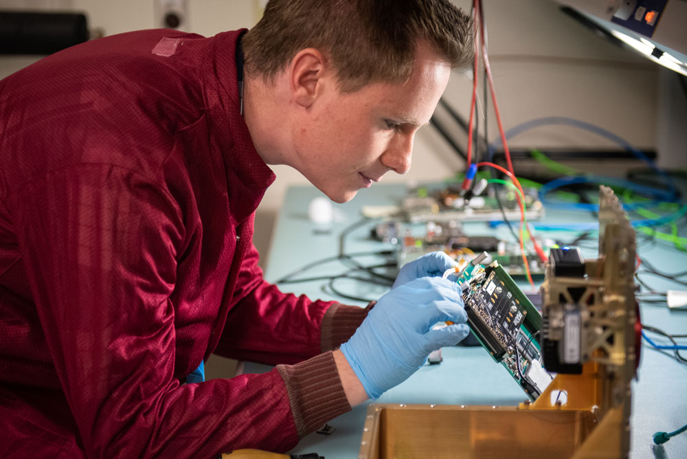 SPACE-BOUND BOARD — Thomas Bradshaw, electrical engineer and flight software lead, inspects a computer board for an upcoming remote sensing mission designed to demonstrate next-generation high-performance computing in space. The team used Valhalla, a Python-based high-performance computing program developed at Sandia, to quickly generate the concept design and estimate mission performance for the payload. (Photo by Craig Fritz)