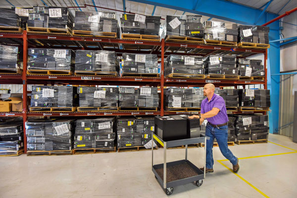 man wheels cart full of computers in warehouse