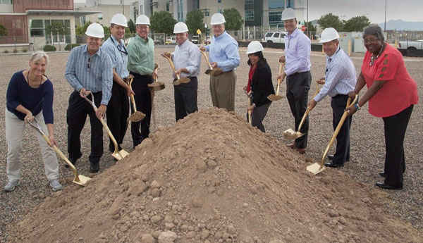 group of people in hard hats with shovels dig into a large pile of dirt