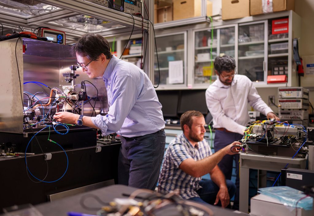 A University of New Mexico joint appointee, left, examines a quantum inertial sensor as engineers initialize controls for a packaged single-side modulator chip.