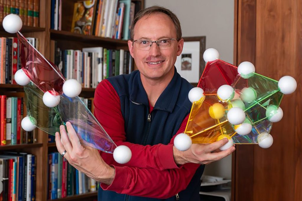 A researcher holds models of 2D and 3D color codes used to produce high-fidelity magic states on a trapped-ion quantum computer.