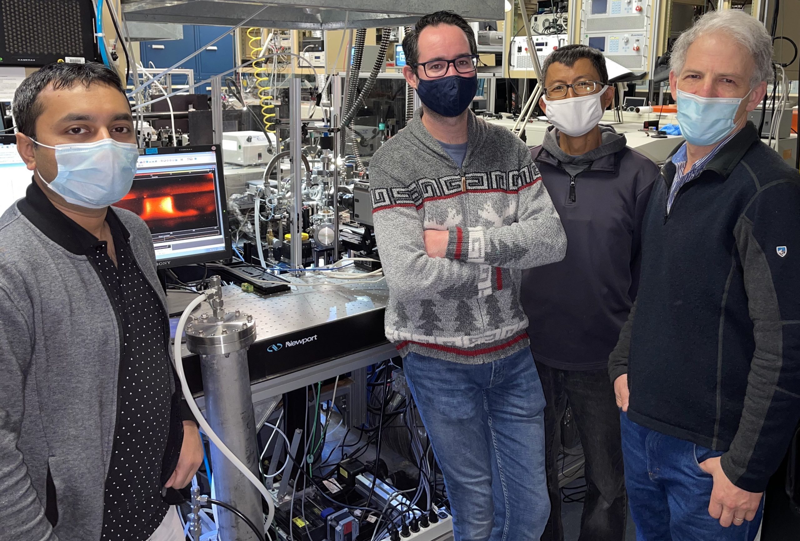 Four people posing for a picture in a lab as part of a team with Jonathan Frank. Instruments behind them