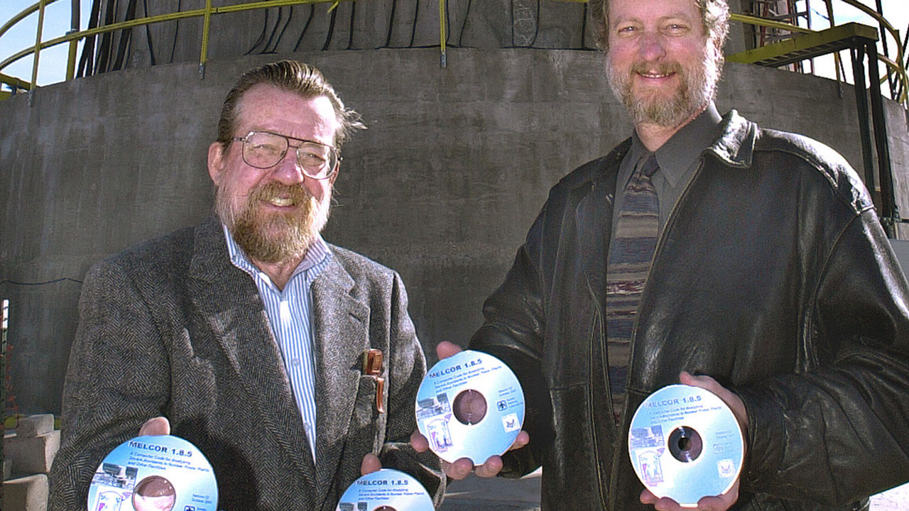 Two men holding copies of MELCOR software on disc