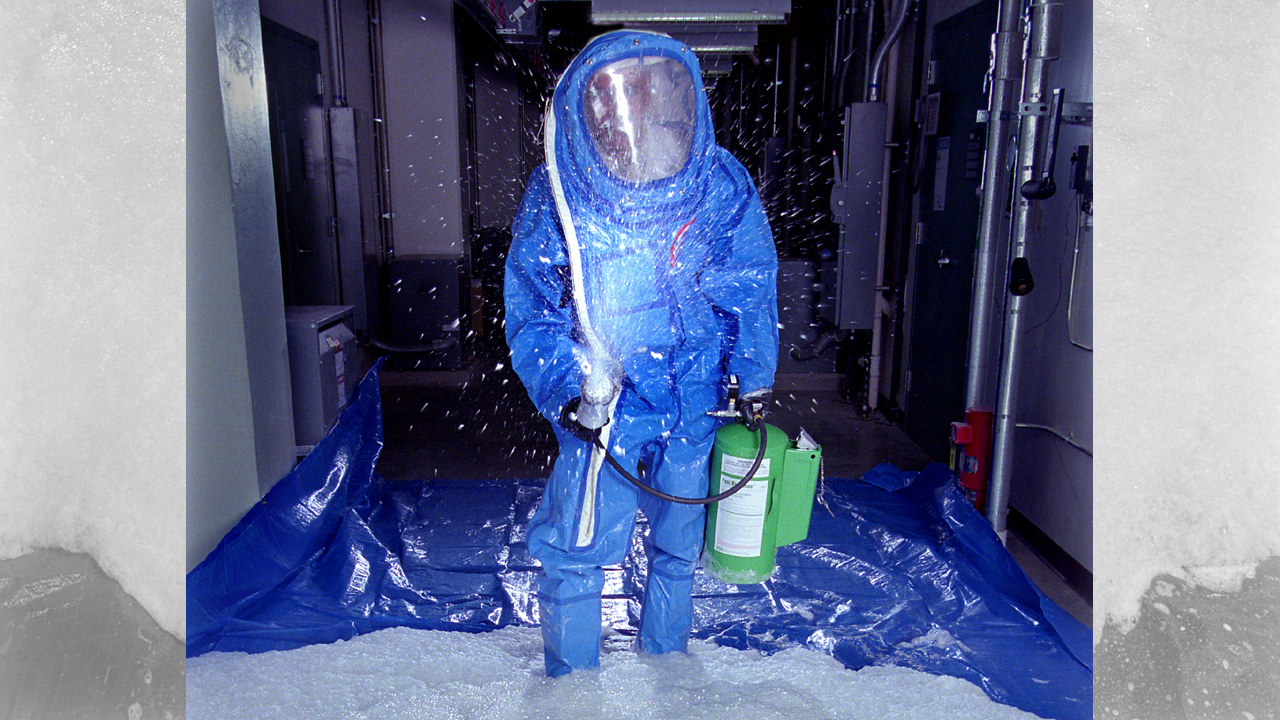 Man in hazard suit spraying decontamination liquid