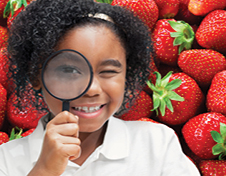 Girl looking through a magnifying glass while standing in front of strawberry background