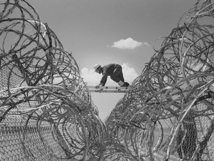 Sandian Bill Ingram scrambles across a perimeter barrier on a ladder in a safeguards exercise, 1977