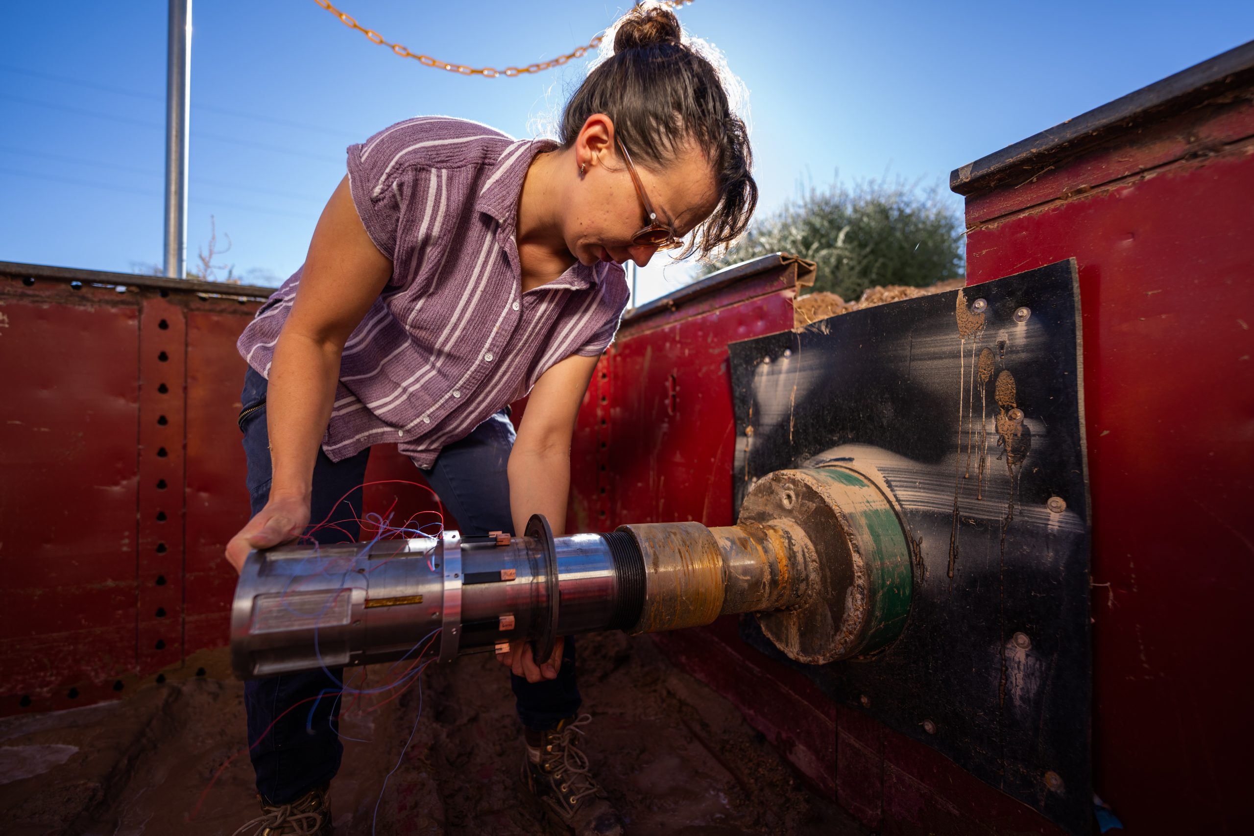 A woman is outside holding a pipe with sensor wires attached.