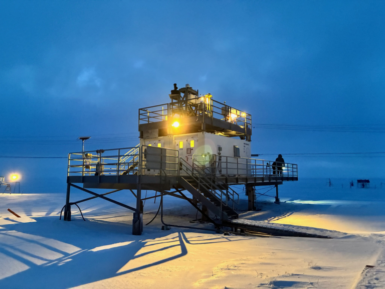 Two people work on top of an open-air platform set in a snowy, dark landscape.