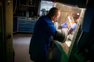 Sandia National Laboratories materials chemist Cody Corbin works in a glove box, preparing a container filled with bead bits that will turn brown if someone attempts to tamper with the container’s contents. (Photo by Craig Fritz) Click on the thumbnail for a high-resolution image.