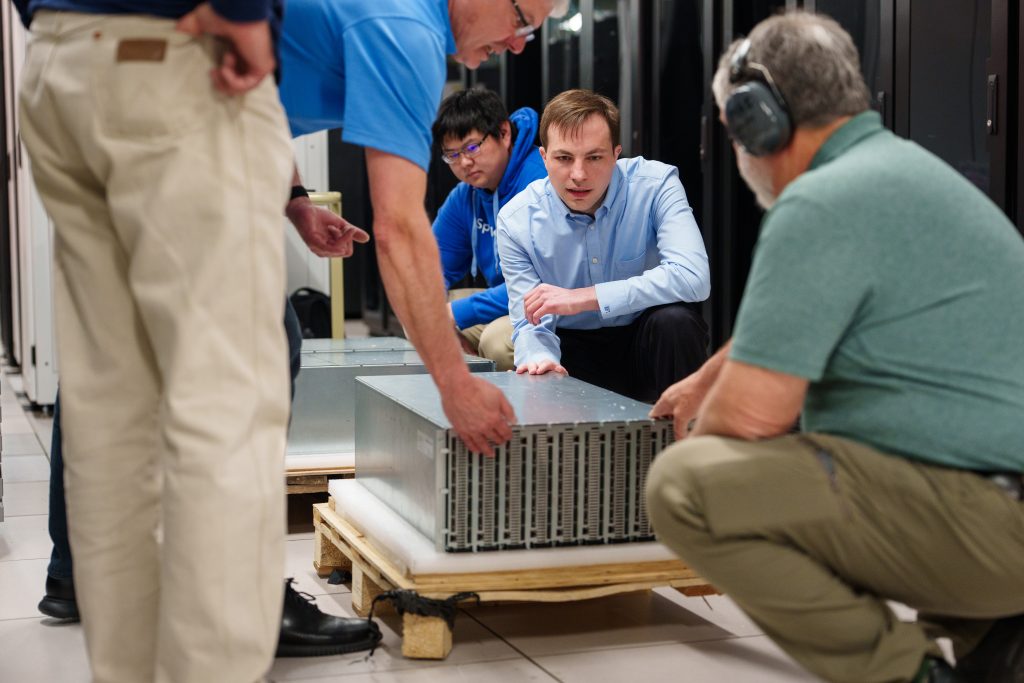 Researchers Brad Theilman, center, and Felix Wang, behind, unpack a neuromorphic computing core at Sandia National Laboratories. While the hardware might look similar to a regular computer, the circuitry is radically different. It applies elements of neuroscience to operate more like a brain, which is extremely energy-efficient. (Photo by Craig Fritz) Click on the thumbnail for a high-resolution image.