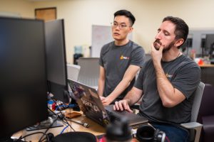 Two men stare at a computer monitor with thoughtful expressions.