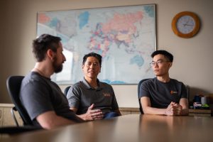 Three men sit in a conference room, discussing.