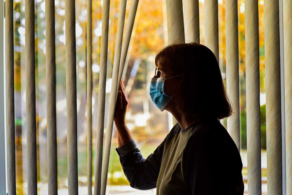 person in mask looks out window