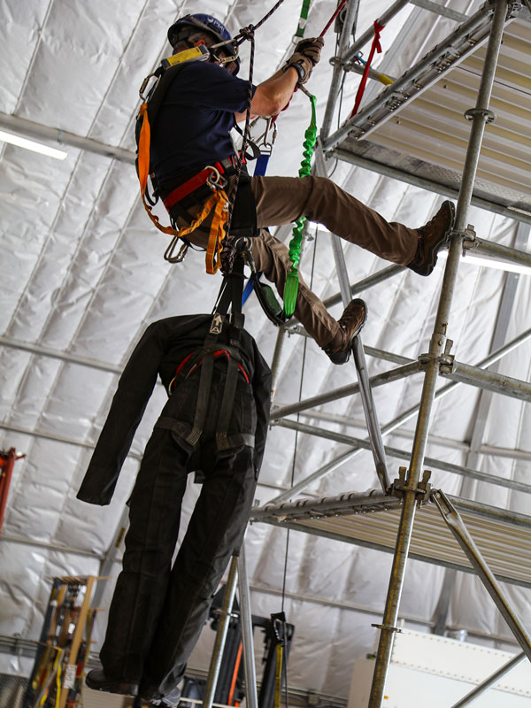 man in harness climbs down scaffolding with rescue dummy