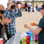 participants wear dark goggles and try to drop oranges in cups