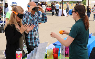 participants wear dark goggles and try to drop oranges in cups