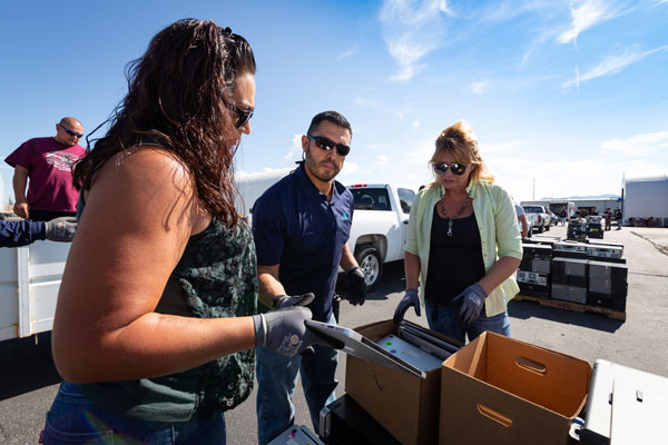 three employees pack laptops into boxes