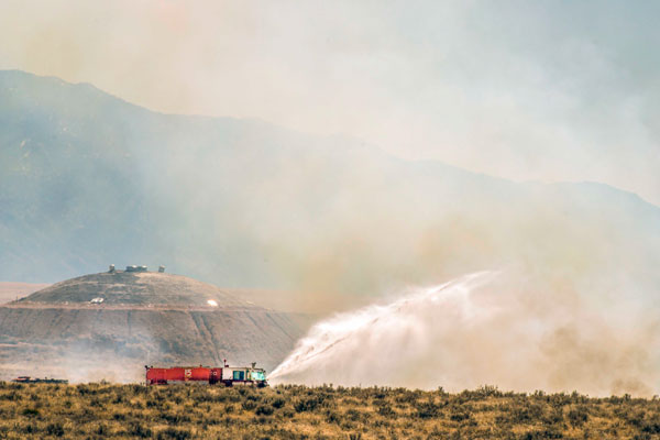 firetruck spraying water on brush fire in remote area of Sandia property