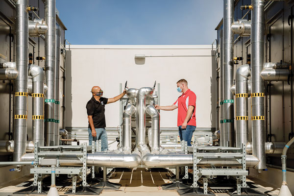 engineers inspect piping on roof of facility