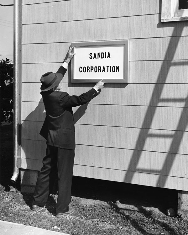 man in suit and derby hat hanging sign outside building