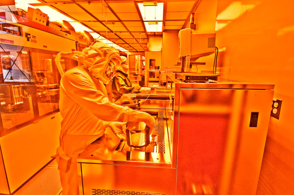 technicians in full protective suits work in lab under glow of orange lights