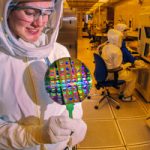 microelectronics technician in HAZMAT suit studies a wafer