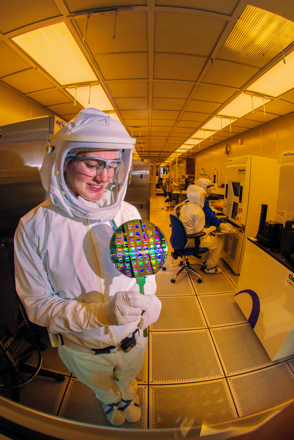 microelectronics technician in HAZMAT suit studies a wafer