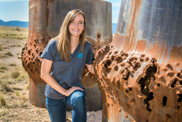 Sandia intern Rebecca Nylen kneels next to blasted steel cylinders