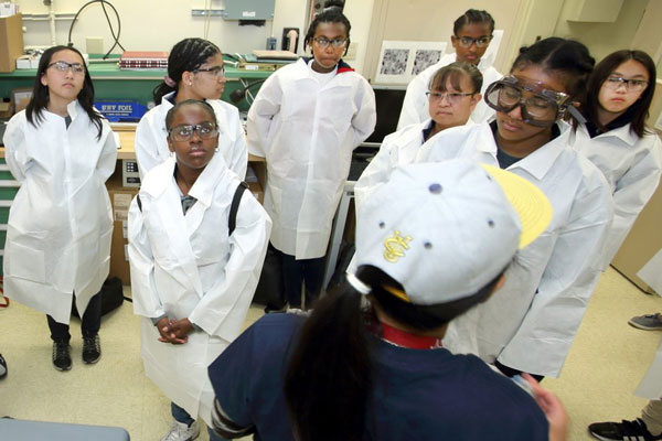 students in lab coats and goggles tour lab