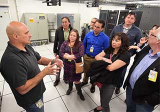 BIG DATA — David Martinez (9324), project lead for Scientific Computing Systems, gives members of the Eastern Band of Cherokees delegation a tour of Sandia’s Data Center. Tribal Vice Chief Richard Sneed (center in the blue shirt) says he was impressed by the center’s water-cooled system. “It’s counterintuitive — water and circuitry — but when you learn how much energy is saved using water to cool everything instead of air, it is just amazing,” he says. (Photo by Randy Montoya)