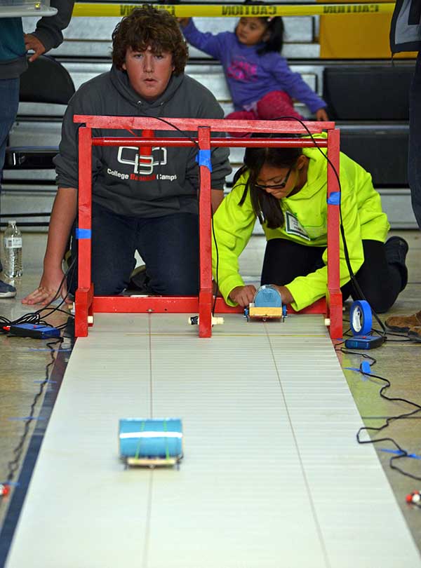 Two students watch as their electric cars race down a 10-meter track during the New Mexico Electric Car Challenge. More than 150 middle school students from across New Mexico participated in the challenge, presented by Sandia National Laboratories, Los Alamos National Laboratory, PNM and Intel.   The challenge, held Nov. 19 at Albuquerque’s Van Buren Middle School, is an annual STEM event in its 10th year. Students formed 5-person teams at the beginning of the school year and were provided basic materials—a lithium-ion battery, a direct-current motor, and other materials such as a chassis and wheels—needed to build their cars.  “Our goal is to expose students to basic engineering. This allows them to see how math and science intersect,” said Amy Tapia, Sandia’s community relations manager.  The teams were also required to give oral presentations on the designs of their cars, as well as the challenges they faced while constructing and running them.