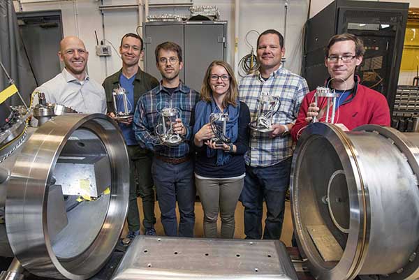 HANDS ON — Posing next to a gas gun open for servicing are, left to right, Sandia shock physicist Seth Root and postdocs Matthew Hudspeth, Joshua Townsend, Bethany Chidester, Jim Williams, and Ray Clay, who are holding the targets they created. (Photo by Randy Montoya)