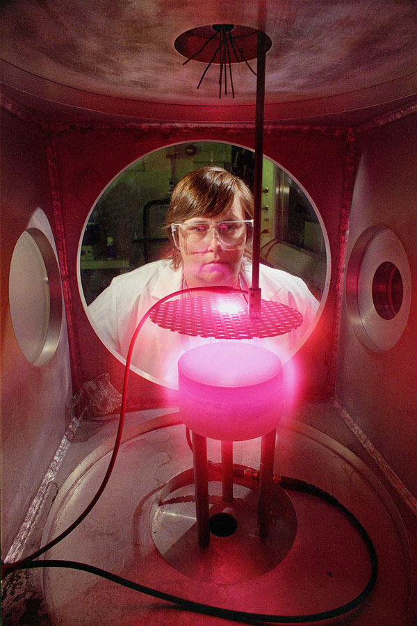 Pam Ward in lab gear looks at glowing pink plasma in case