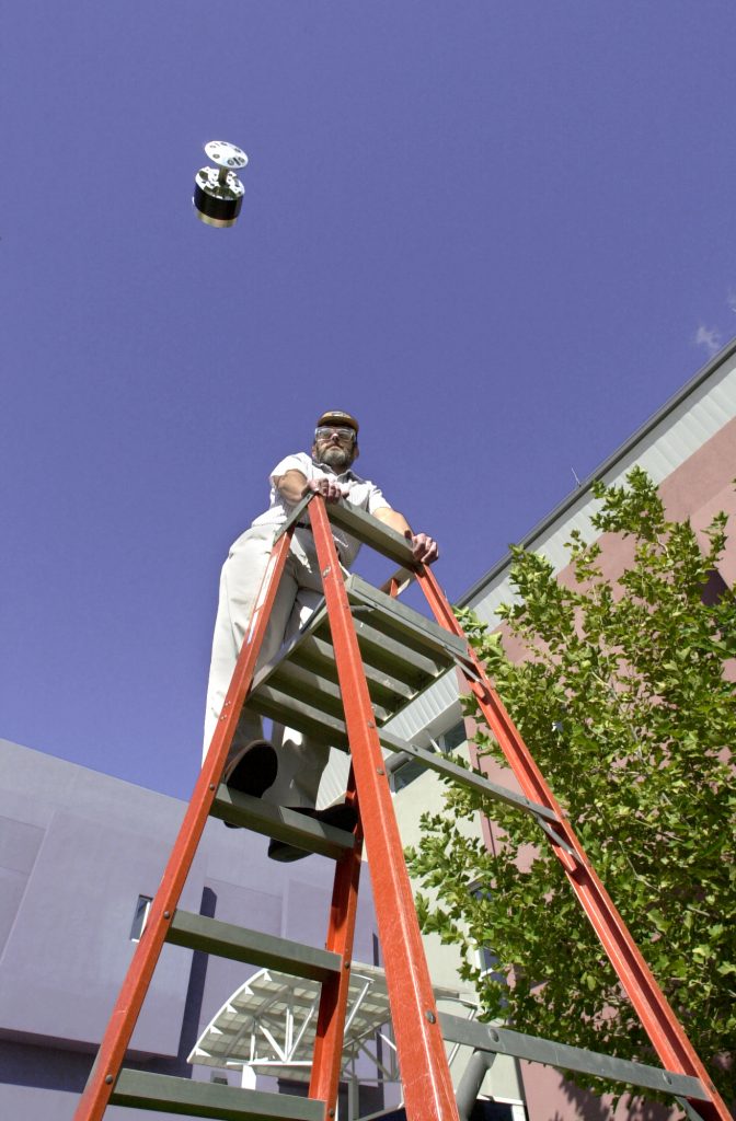 Man at the top of a ladder watching the hopper robot jump by him. 