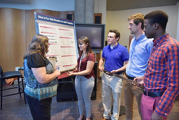 Diane Peebles, manager of Component Science and Mechanics Dept. 1556, talks with NOMAD participants about their summer work in nonlinear dynamics. The students hold examples of the two bolted-together steel bars they analyzed during the program.