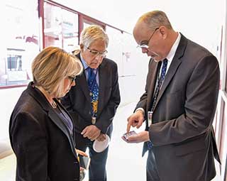 During a tour of Labs facilities and briefings on key mission area work, Center 1700 Director Dave Sandison, right, shows US Rep. Michelle Lujan Grishman a component produced in Sandia’s MESA facility as Div. 6000 VP Jim Chavez looks on.