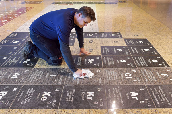 Man polishing periodic table inlaid on museum floor