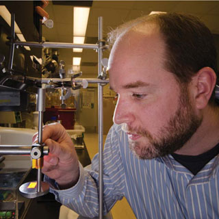 Image of <p>Organic materials chemist Shawn Dirk (1821) focuses a projector during work on neural interfaces, which are aimed at improving amputees’ control over prosthetics with direct help from their own nervous systems. Focusing prior to exposing polymers ensures that researchers pattern the desired feature sizes for the interfaces.  (Photo by Randy Montoya) <a href="/news/publications/labnews/archive/_assets/images/12-24-02/pic1lg.png">View large image</a>. </p>
