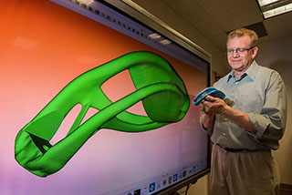 Topology optimization achieved the unique shape of the lantern bracket held by Ted Blacker (1543) and displayed in the topology optimization program behind him. The computer program started as a square block and, following parameters set by a designer, drew I-beam-like supports and plates with filleted attachments to reduce stress concentrators where one member meets another. (Photo by Randy Montoya)