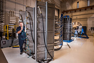 Sandia technician Tommy Mulville installs a gas exhaust line for a switch at Thor’s brick tower racks. In the background, beyond the intermediate support towers, technician Eric Breden makes ready an electrical cable for insertion in the central power flow assembly. (Photo by Randy Montoya)
