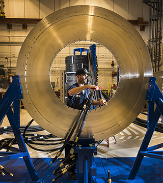 MAKING READY FOR THOR — Sandia tech Eric Breden terminates a transmission cable for installation on the silver disk that is the new pulsed-power machine’s central powerflow assembly. (Photo by Randy Montoya)