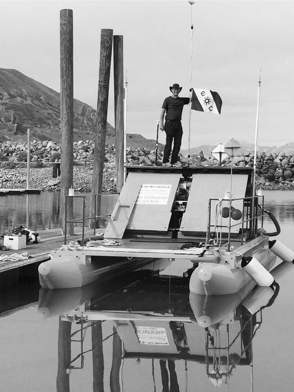 AHOY, DARK MATTER — Pace VanDevender, former vice president for science and technology, poses with the expedition flag of the Explorer Club of New York City atop his original floating dark matter sensor, docked at the Great Salt Lake, Utah. (Photo courtesy of Pace VanDevender)