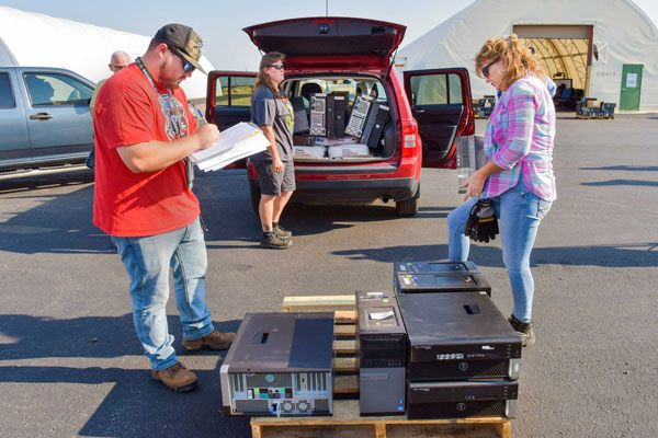 TECHNOLOGY TRANSFER — Reapplication team employee Marcus Barela (left) records property information prior to its release from Sandia. Bernadette Bazen (center) and Semiramis Novak, also on the Reapplication team, help load desktop computers into a vehicle for one of the schools.