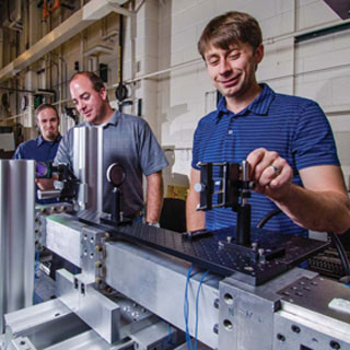 UNIQUE MACHINE — Steve Beresh (1515), Sean Kearney (1512), and Justin Wagner (1515), left to right, are part of a team that developed Sandia’s multiphase shock tube. The 22-foot-long machine, which uses various diagnostics, makes it possible to study how densely clustered particles disperse during an explosion. (Photo by Randy Montoya)