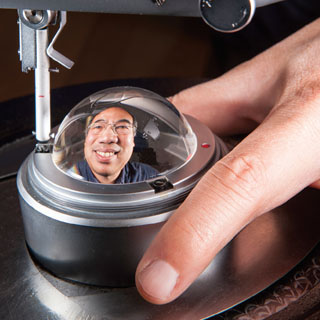 REALLY ROUND — The image of project lead Hy Tran (2541) is reflected in a polished quartz ball that is the standard for roundness. The Primary Standards Laboratory at Sandia uses a specialized instrument to measure roundness deviation against the roundness standard, which has been certified to national standards to be round within about 20 nanometers. (Photo by Randy Montoya)