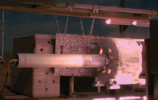 IMPACT TEST — A rocket sled (entering the frame from the right side of photo) slams into a stationary B61-12 mock weapon at the end of Sandia’s 10,000-foot sled track during a successful test last month. Tests in July and August marked the return of supersonic testing to the Rocket Sled Track. (Photo courtesy of Ed Bystrom, Dept. 1535)