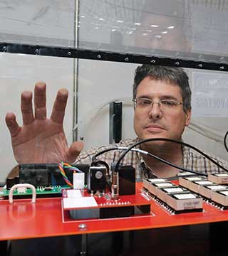 Caption: BOB KAPLAR (1768) peers at a test circuit built under a Grand Challenge Laboratory Directed Research and Development project to evaluate the switching performance of wide bandgap and ultra-wide bandgap power semiconductor devices. (Photo by Randy Montoya)