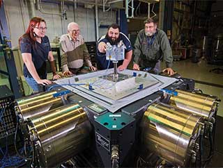 GOOD VIBRATIONS — Sandia 6DOF research team member Kevin Cross (1521), second from right, adjusts accelerometer cables on a block head test item as, from left, Davinia Rizzo (1557), David Smallwood, and Norman Hunter look on. The team is working with a new type of large vibration machine capable of shaking test items in multiple directions simultaneously. The block head is a dynamically active structure designed to challenge the team’s ability to control a complex system. (Photo by Randy Montoya)